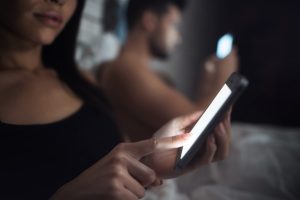 Um Casal Deitado Na Cama à Noite, Ambos Usando Um Celular Enquanto Parecem Relaxados E Apaixonados.