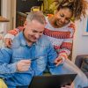 Um Casal Interracial Feliz Sentado Em Um Sofá, Desfrutando De Compras Online Juntos Em Sua Casa.