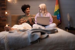 Um Casal Lésbico Sentado Junto, Olhando Para Um Laptop, Sorrindo E Envolvidos Em Uma Conversa, Simbolizando O Papel Da Tecnologia Na Promoção Da Inclusão Sexual.