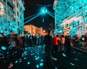 Uma Rua Movimentada Da Cidade à Noite, Cheia De Pessoas Socializando, Iluminada Por Luzes Coloridas Dos Prédios E Letreiros Ao Redor.