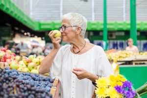 Uma Mulher Idosa Selecionando Frutas Frescas Em Um Mercado Ao Ar Livre, Sorrindo Enquanto Observa Os Produtos.