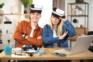 Um Jovem Casal Está Sentado No Sofá, Ambos Usando óCulos De Realidade Virtual E Interagindo Com Um Laptop, Indicando O Uso De Tecnologia Em Produtos Para Adultos.